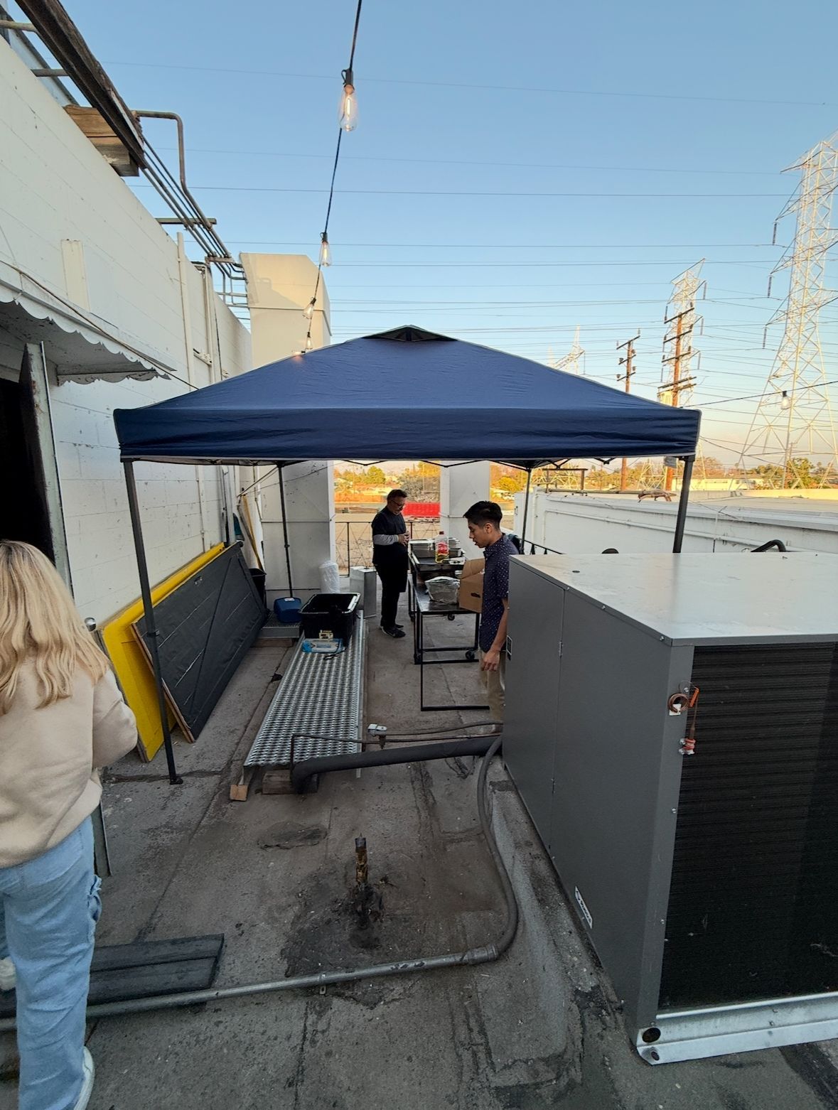 A man is standing under a blue tent on the roof of a building.