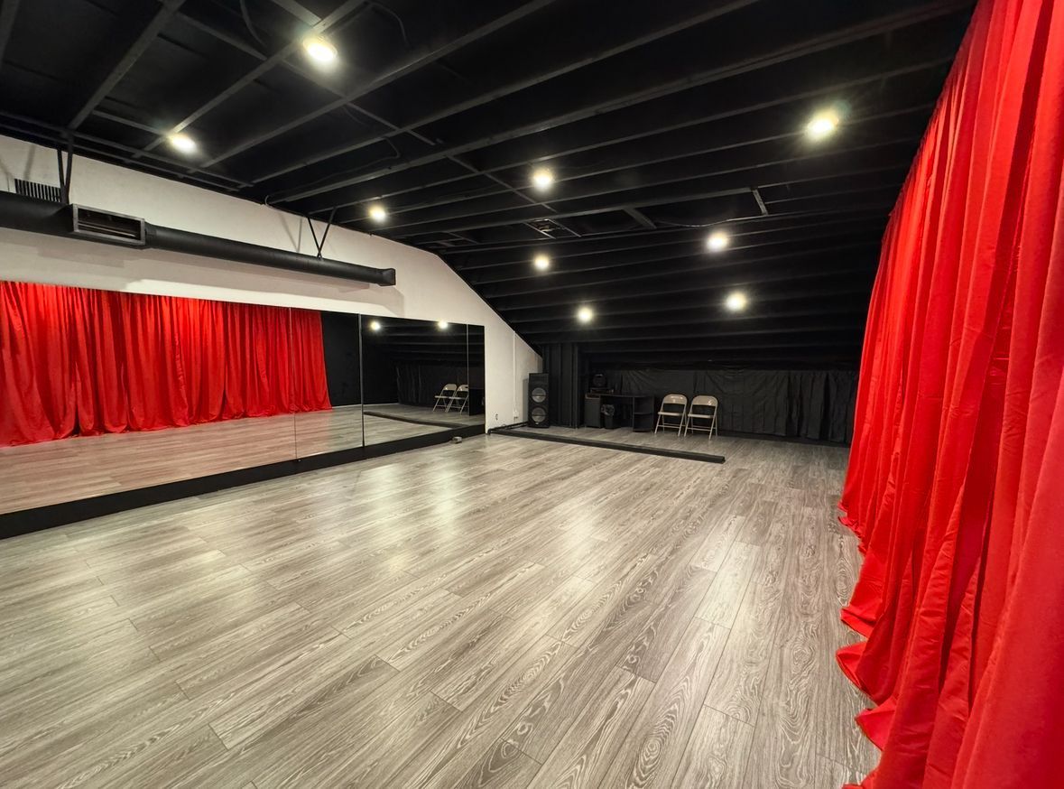 An empty dance studio with a large mirror and red curtains.