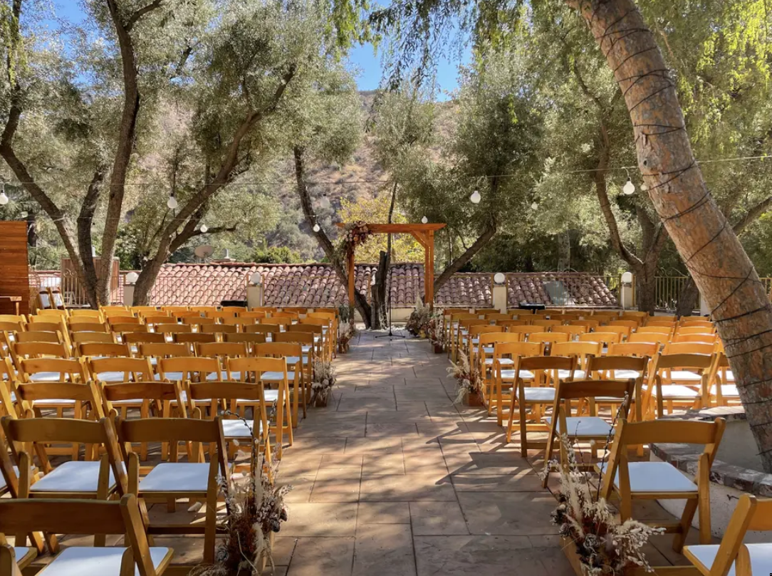 Outdoor wedding ceremony setup with rows of wooden chairs lining a stone aisle under trees