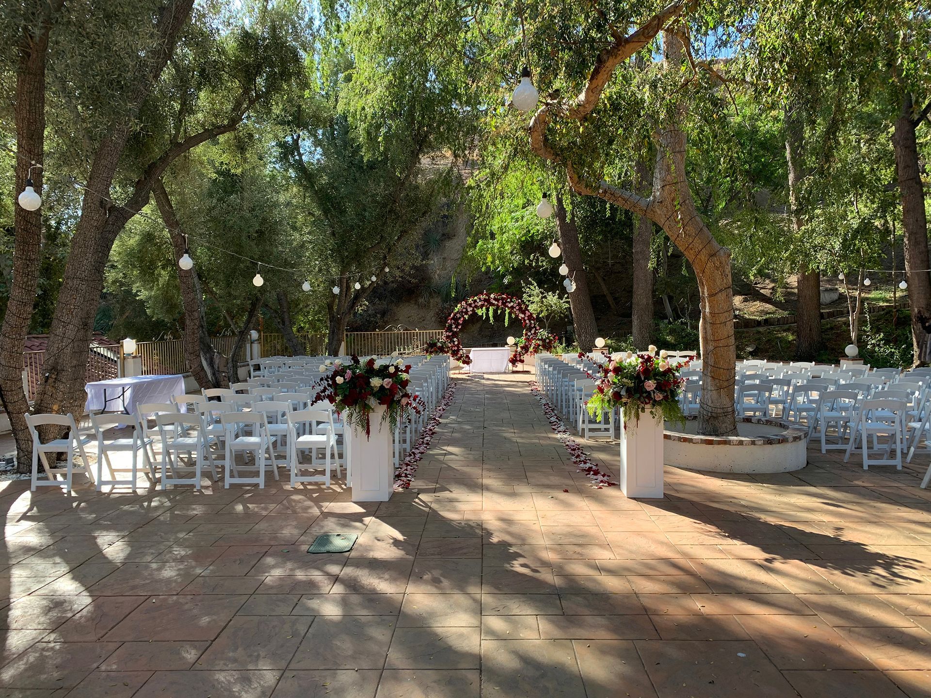 Outdoor wedding aisle with white chairs and flower arrangements under trees