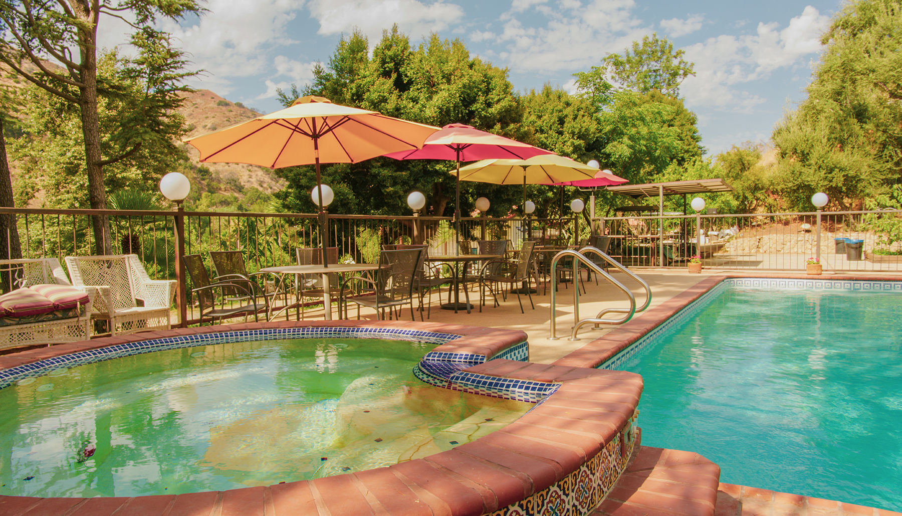 Outdoor pool with hot tub, lounge chairs, and colorful umbrellas in a sunny resort setting