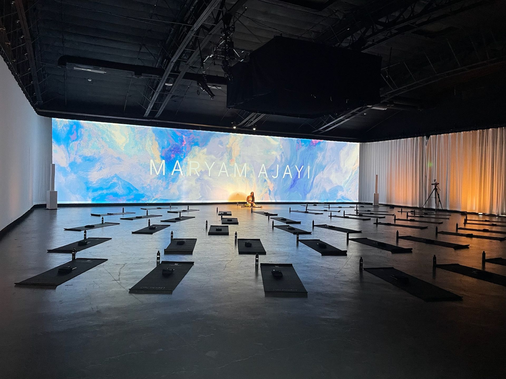 An empty yoga studio with rows of mats on the floor, facing a large screen displaying 