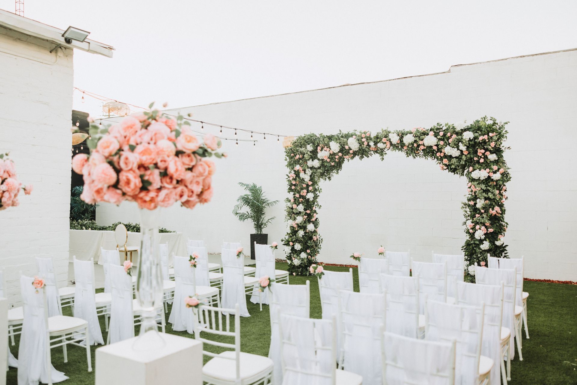 A row of white chairs and a floral arch for a wedding ceremony.