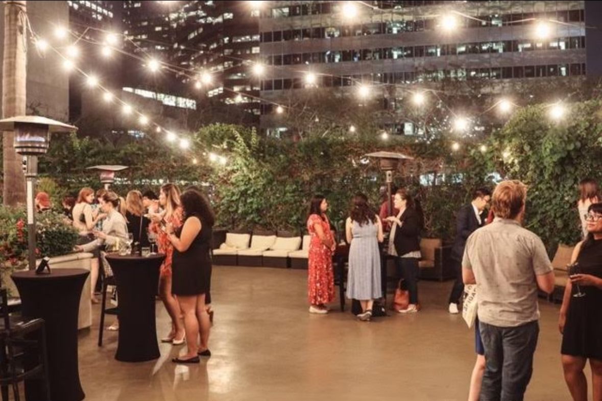 A group of people are standing around tables and talking at a party.