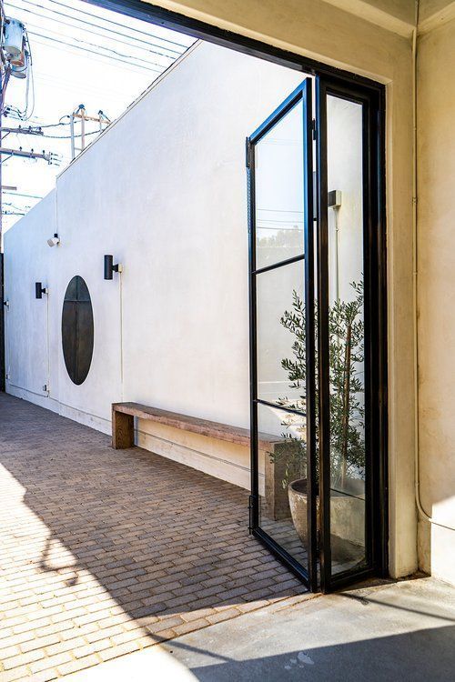 A glass door is open to a brick walkway with a bench in the background.