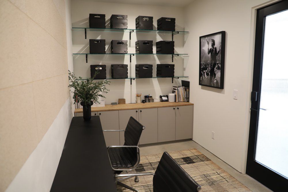 A home office with a desk , chair , shelves and a picture on the wall.