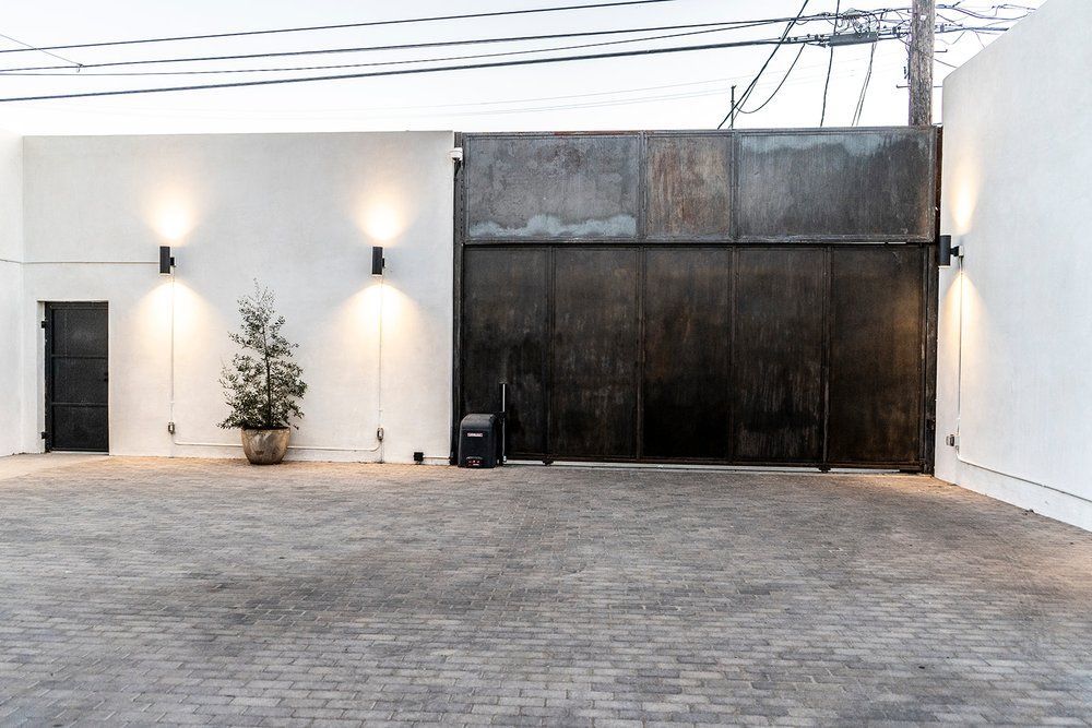 A brick driveway leading to a white building with a metal gate