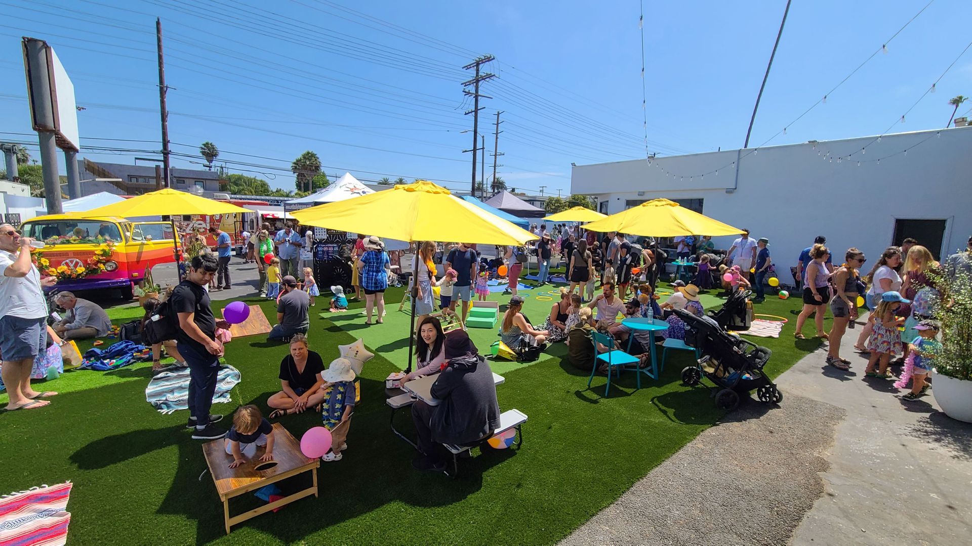 A large group of people are sitting under yellow umbrellas in a grassy area.