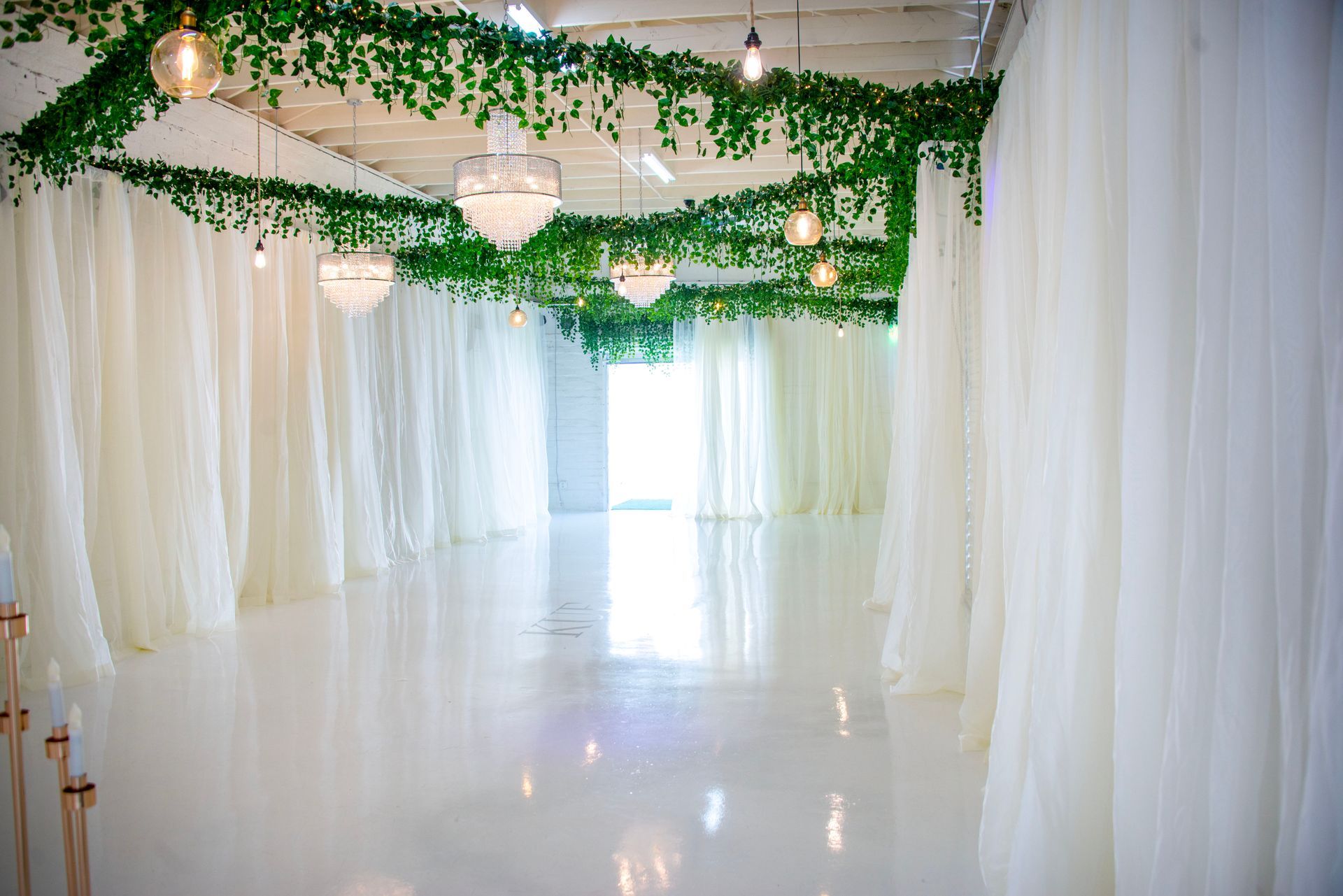 A long hallway with white curtains and green ivy hanging from the ceiling.