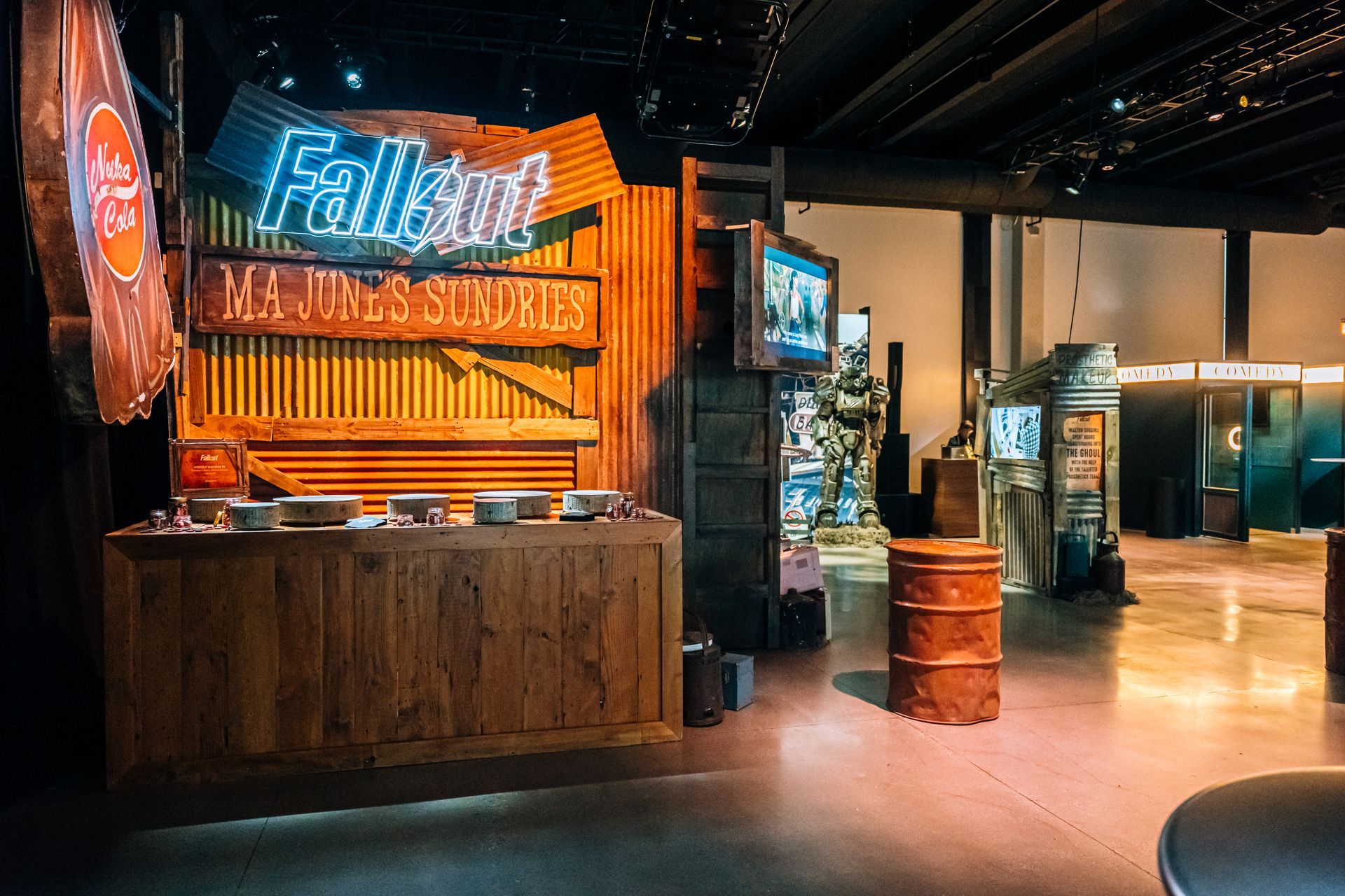 A Fallout-themed display at a museum, featuring a wood counter, neon sign, and a power armor suit in a dimly lit hall.