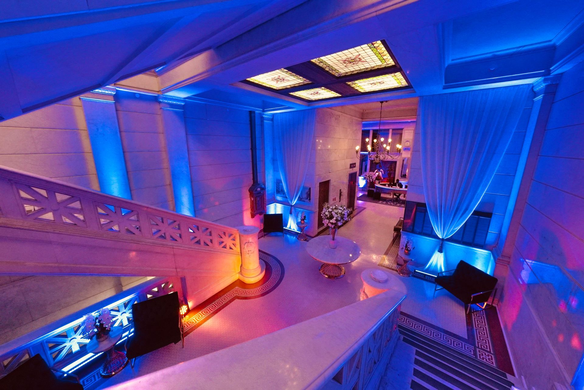 A grand, white staircase leads to a modern, multi-level lobby bathed in vibrant blue and magenta neon mood lighting.