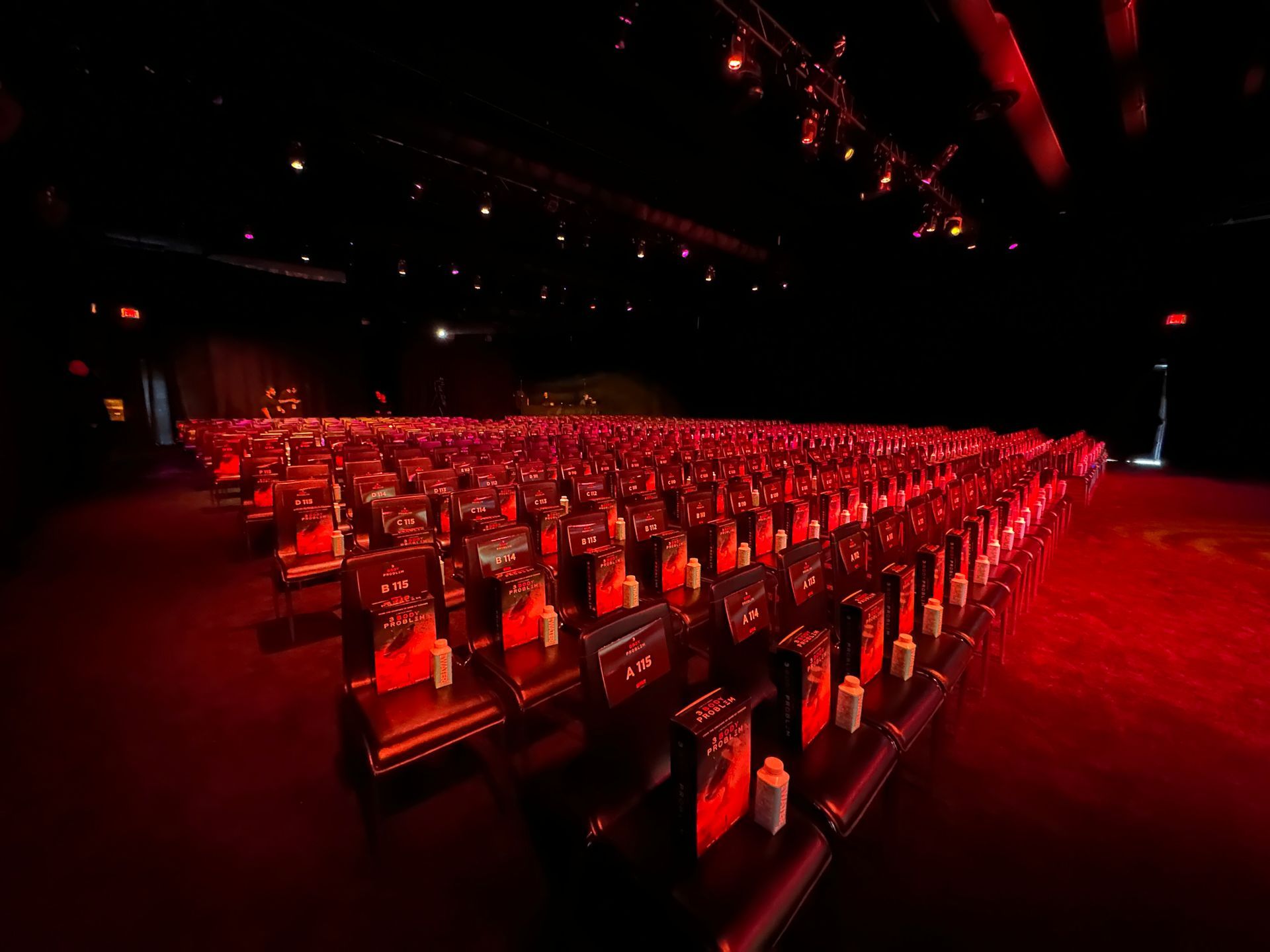 Rows of empty red-lit theater seats facing a dark stage.