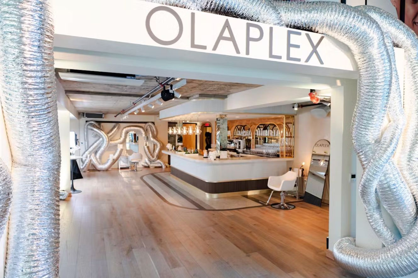 A modern salon space featuring an Olaplex sign at the entrance, framed by silver, winding decorative tubes.