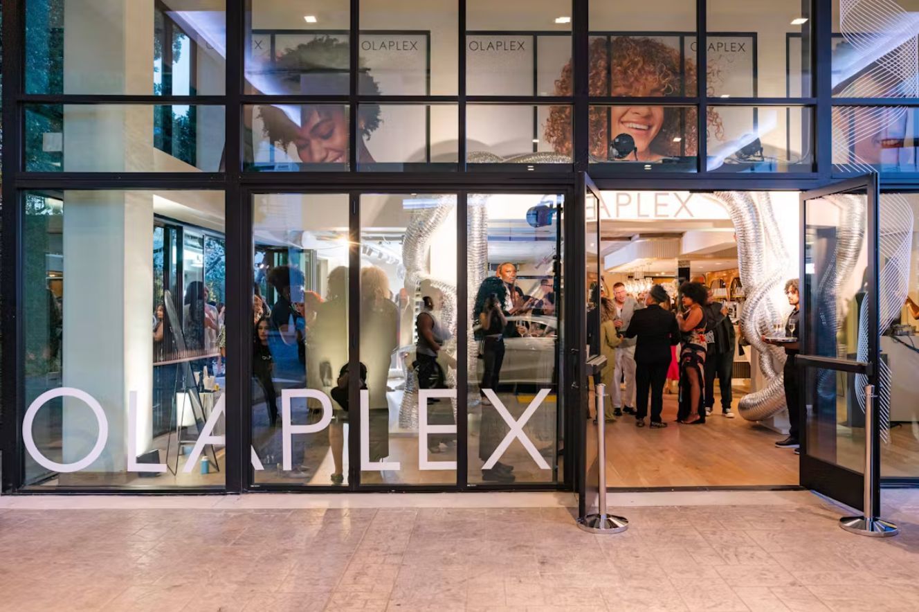 The entrance to an Olaplex brand building, featuring glass doors and large white lettering against an illuminated interior.