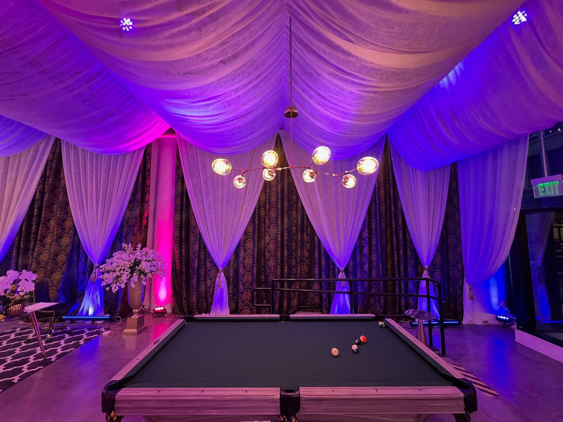 Purple-lit banquet hall with draped ceiling and a pool table in the center
