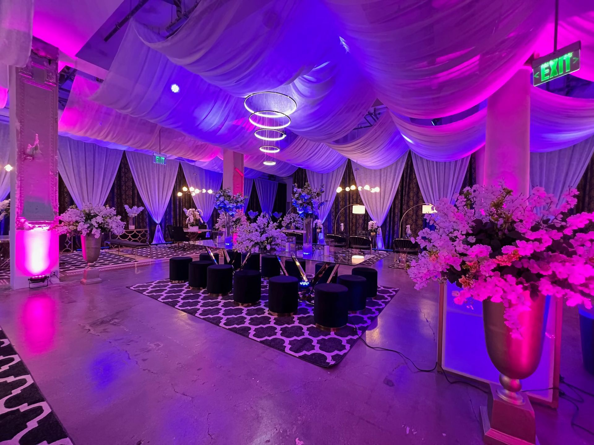 Elegant banquet hall with purple lighting, draped ceiling, round tables, and floral centerpieces