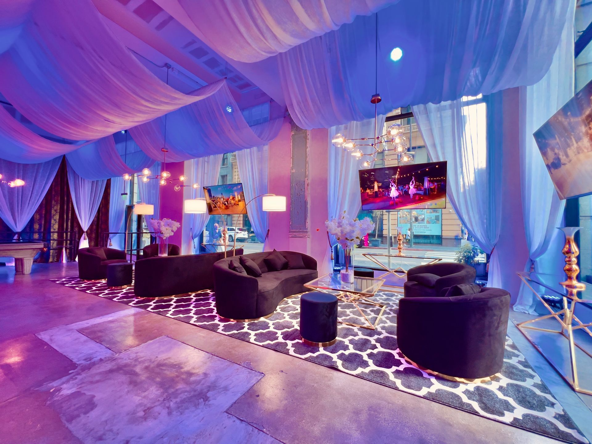 Luxurious lounge with draped blue-purple ceiling, patterned carpet, round ottomans, and large windows overlooking water