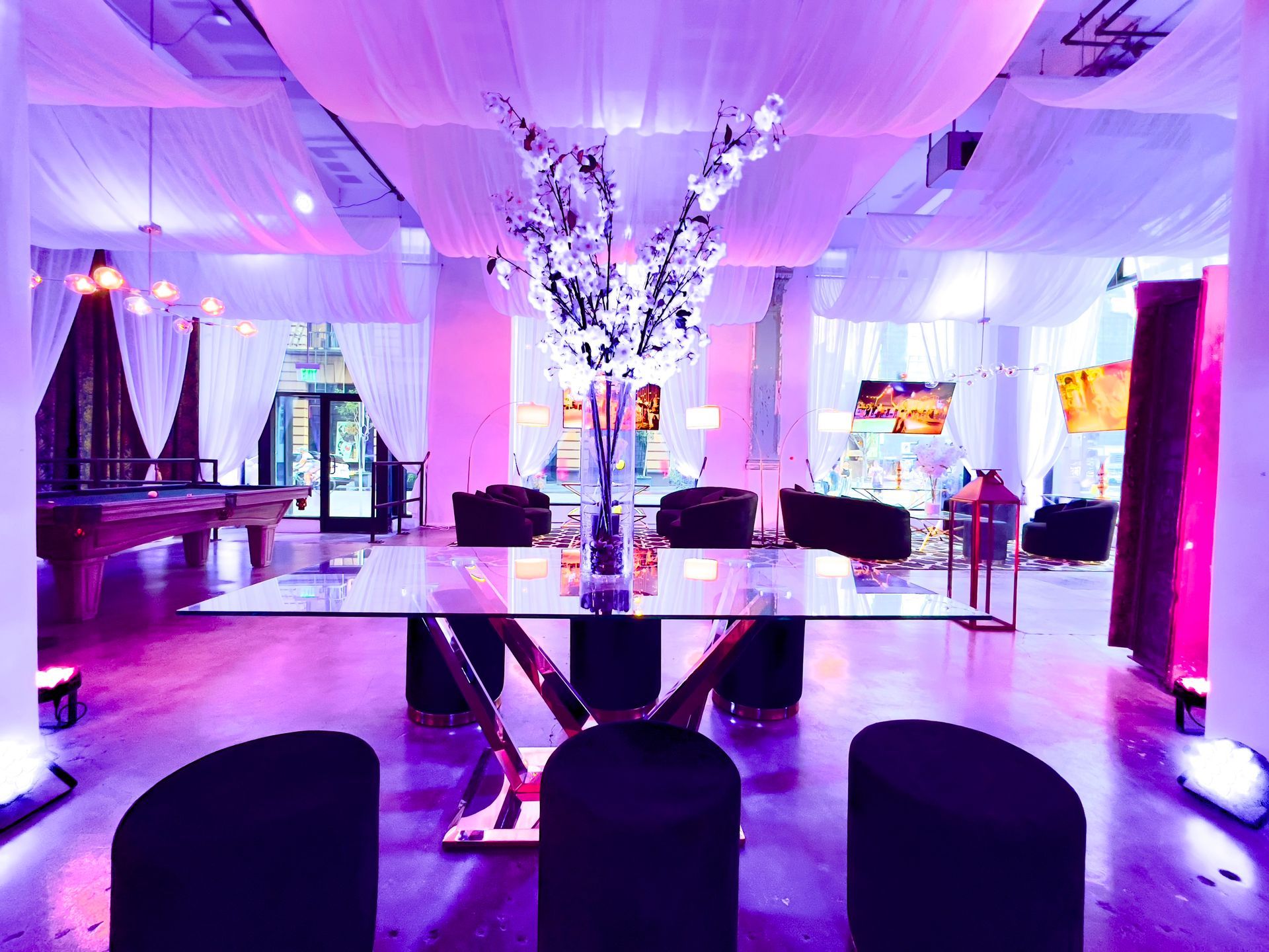 Elegant banquet hall with purple lighting, mirrored tables, and black chairs around a central floral display