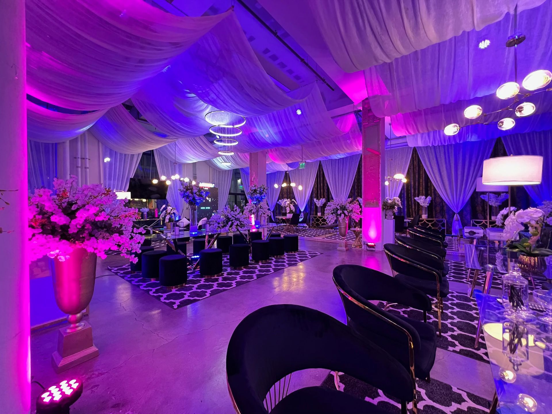 Lavishly decorated event venue with purple lighting, draped ceilings, floral arrangements, and modern chairs