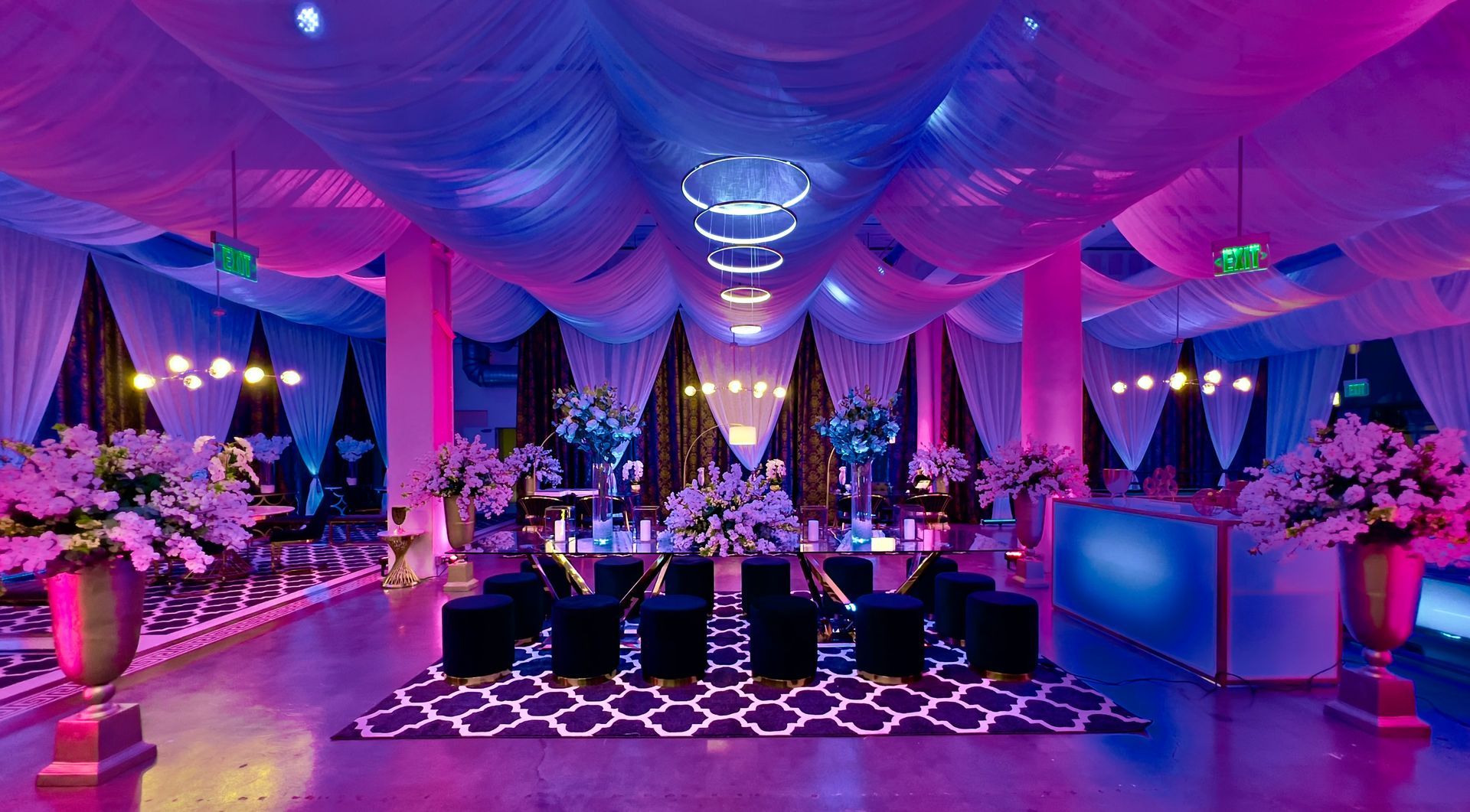 Lavishly decorated event hall with purple-blue lighting, draped ceiling, floral arrangements, and seated guests