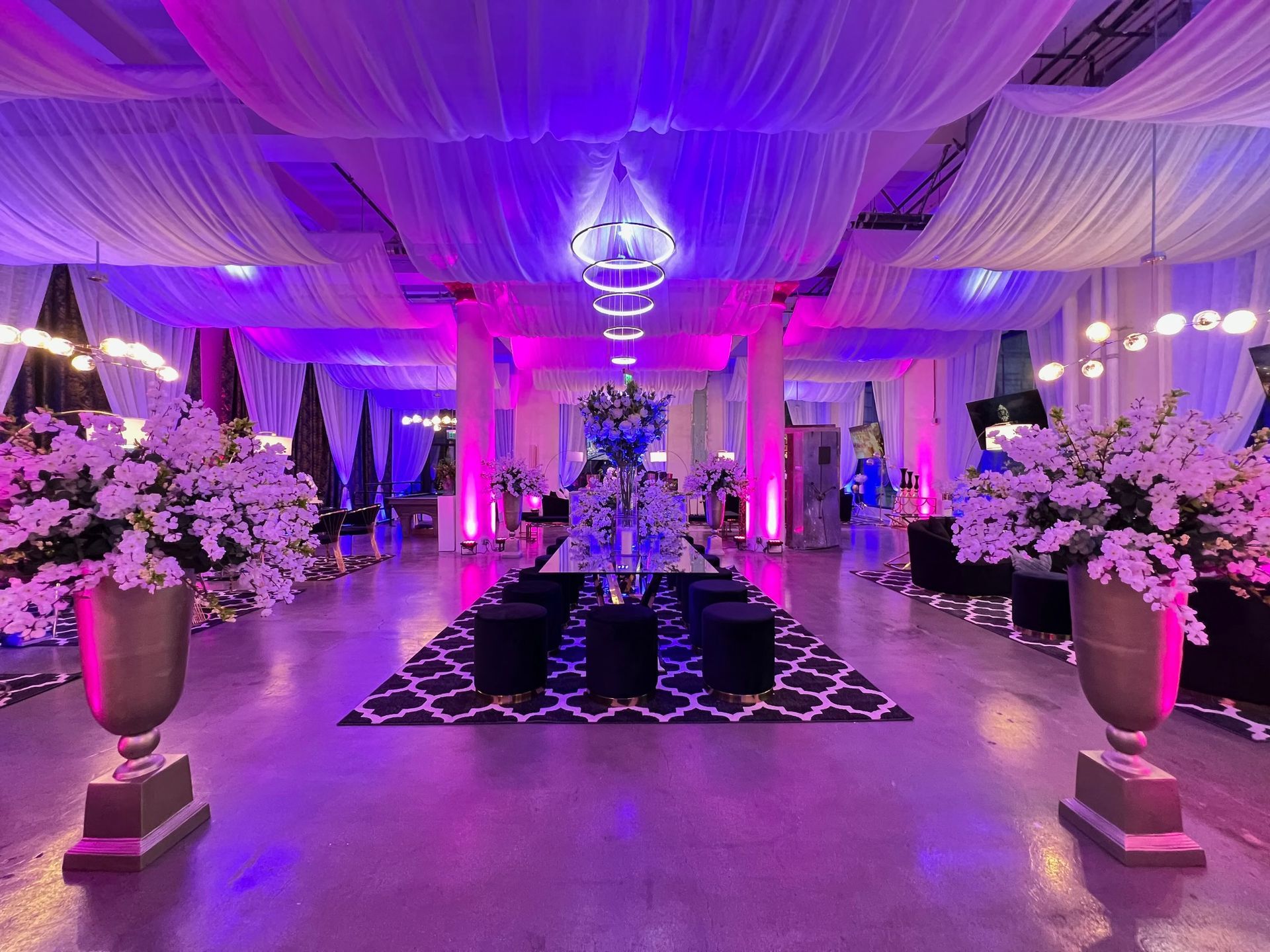 Lavishly decorated banquet hall with purple lighting, draped ceiling, floral centerpieces, and a patterned aisle