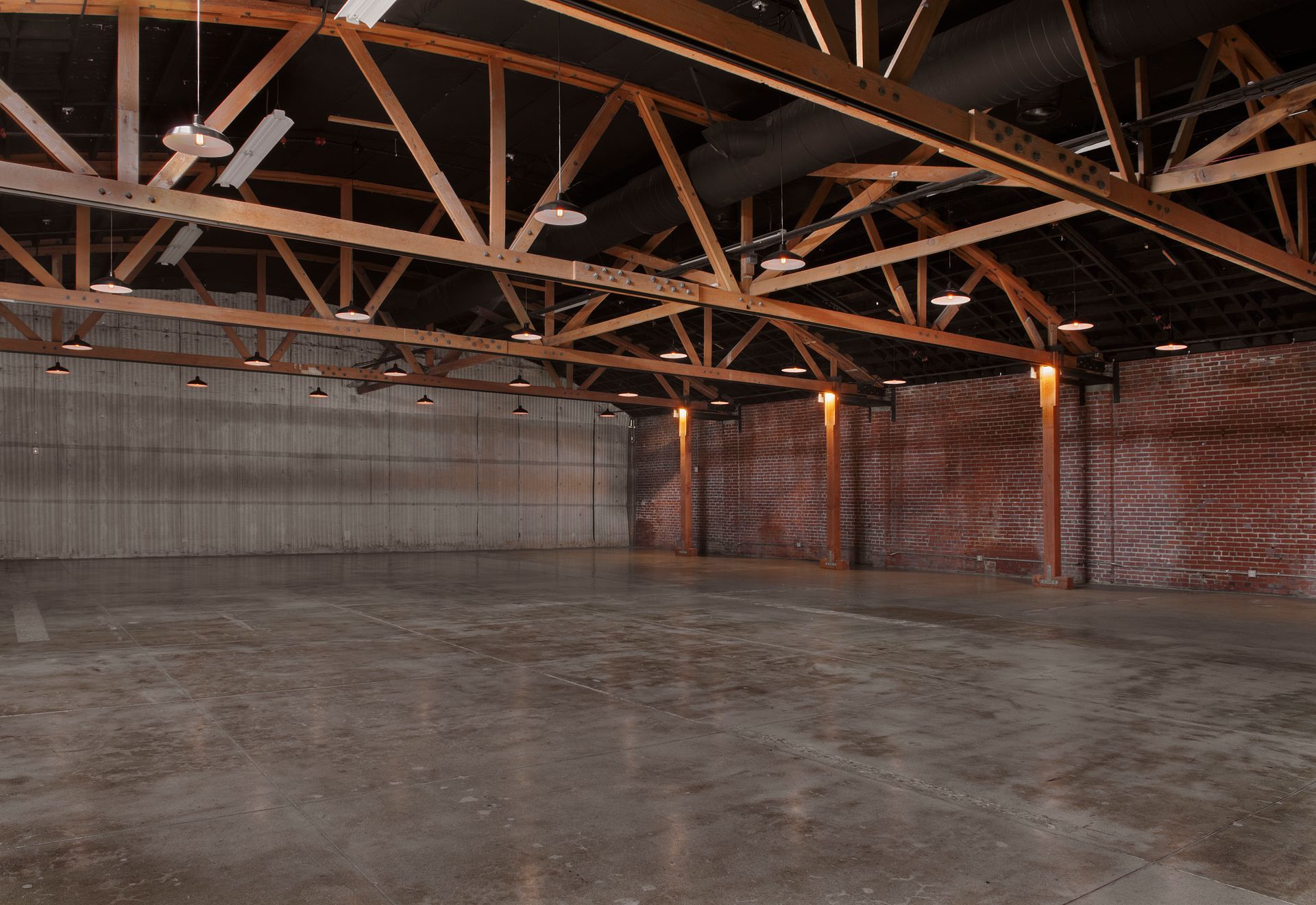 An expansive, empty industrial event space with high wooden truss ceilings, concrete floors, and brick and concrete walls.
