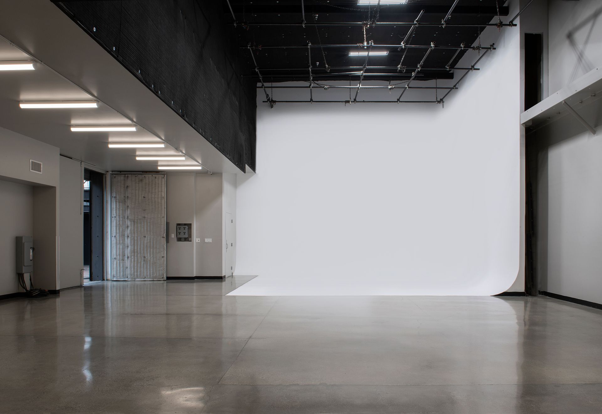 A modern, spacious photography studio with a white cyclorama wall, polished concrete floors, and overhead grid lighting.