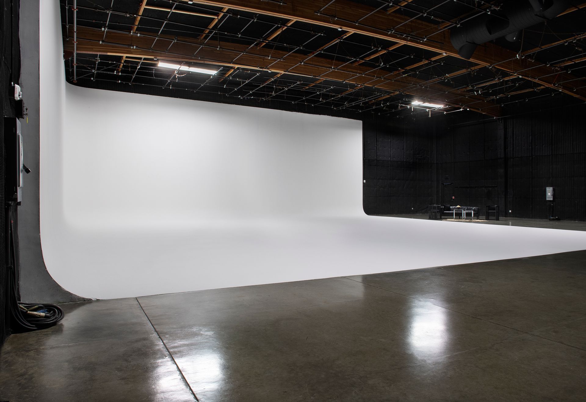 A wide-angle interior view of a spacious photography studio featuring a large, curved white wall and a polished concrete floor.