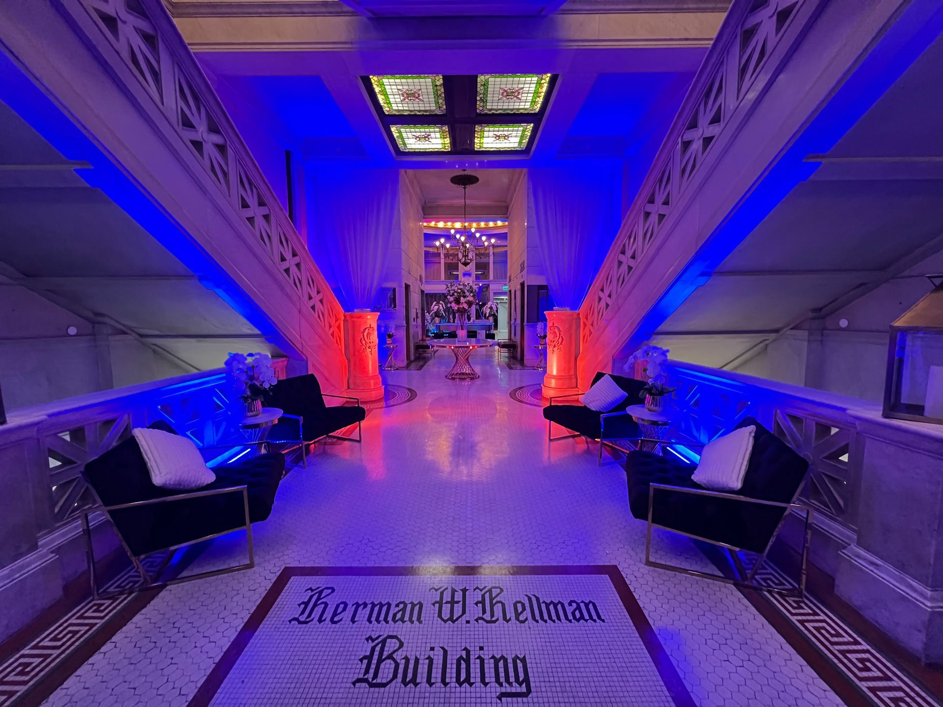 The lobby of the Herman W. Hellman Building with ornate stairs, black chairs, and dramatic blue and red lighting.