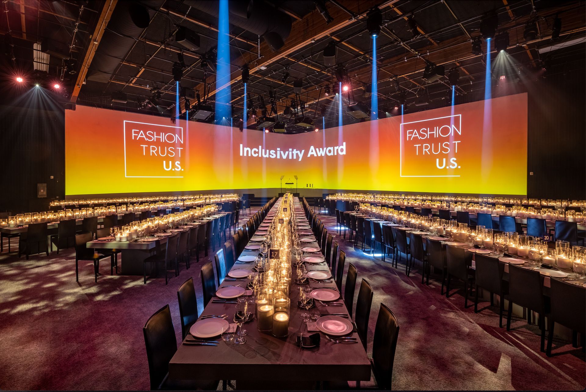 A long dinner table set for an event with bright, golden stage backdrops labeled 