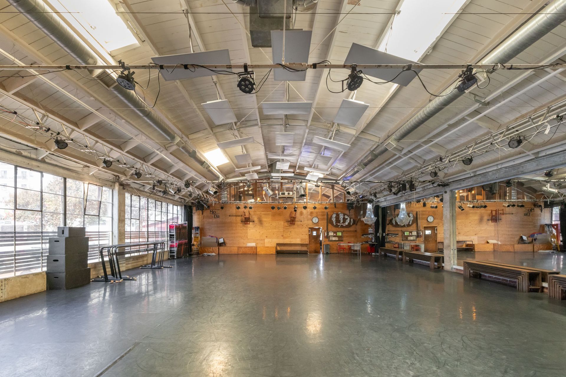 Large, open industrial event space with a concrete floor, wooden walls, high vaulted ceiling, and stage lighting fixtures.