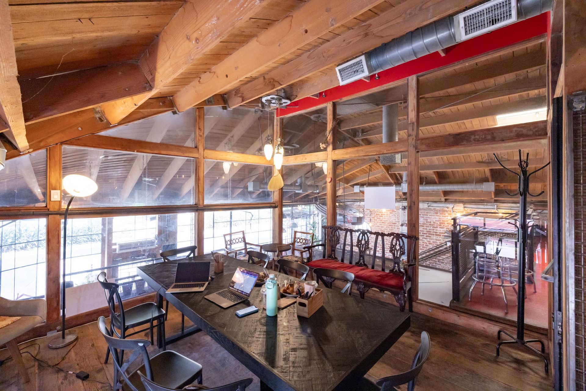 An open-concept loft workspace with a long dark table, several chairs, computers, and visible wooden ceiling beams.