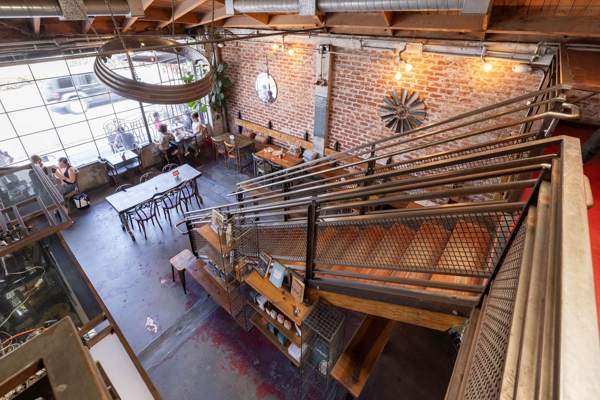 A high-angle view of a rustic, industrial-style restaurant interior with a metal staircase, brick walls, and seating.