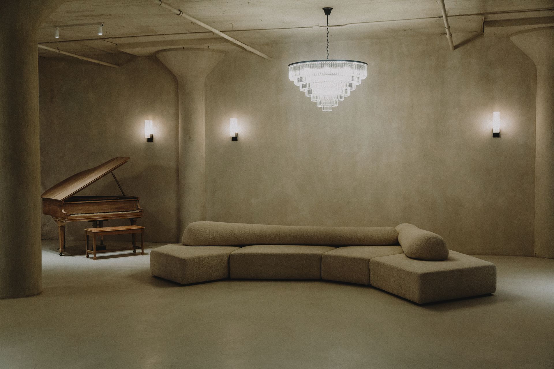 A living room with a couch , piano and chandelier.