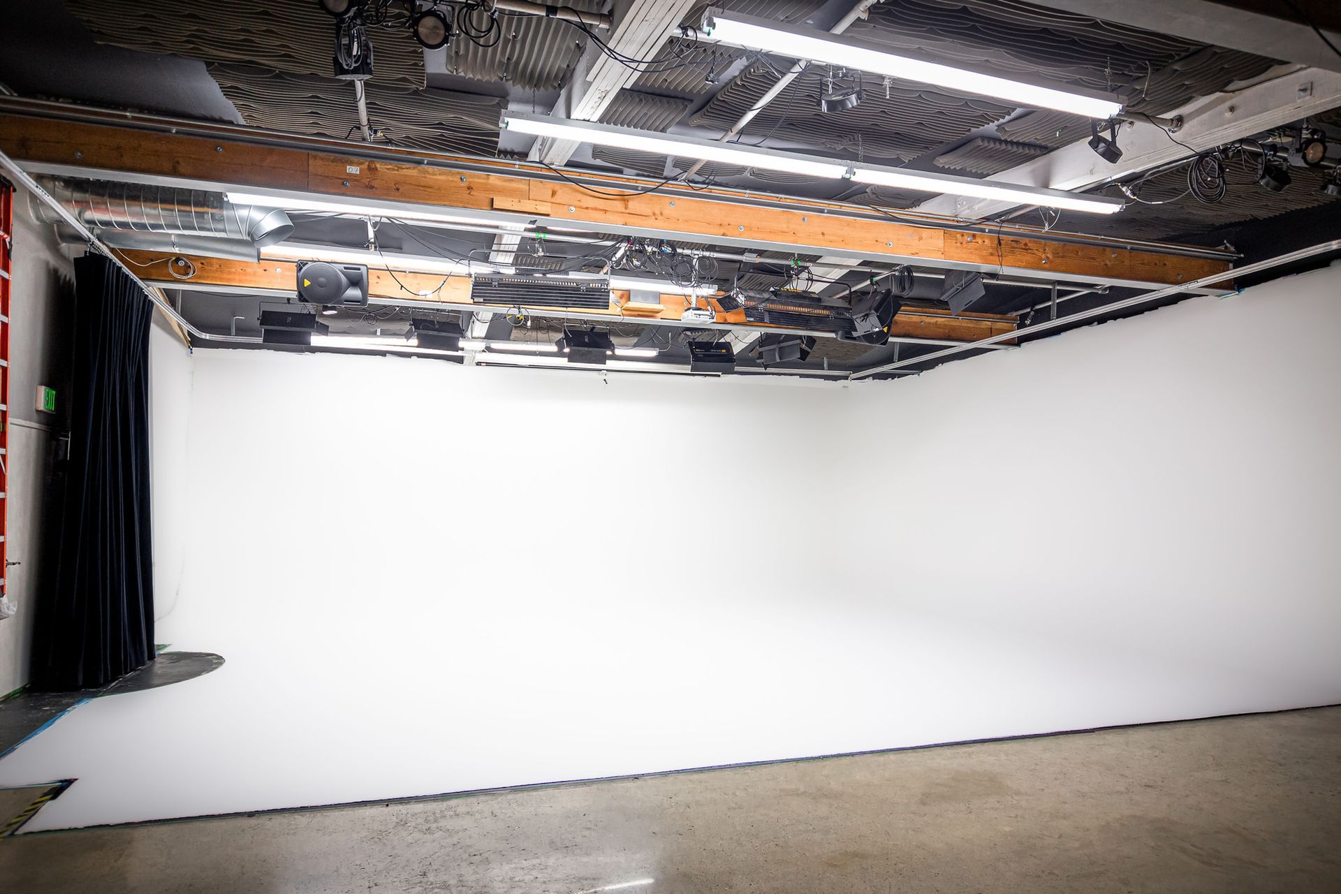 An empty room with a white wall and a black curtain hanging from the ceiling.