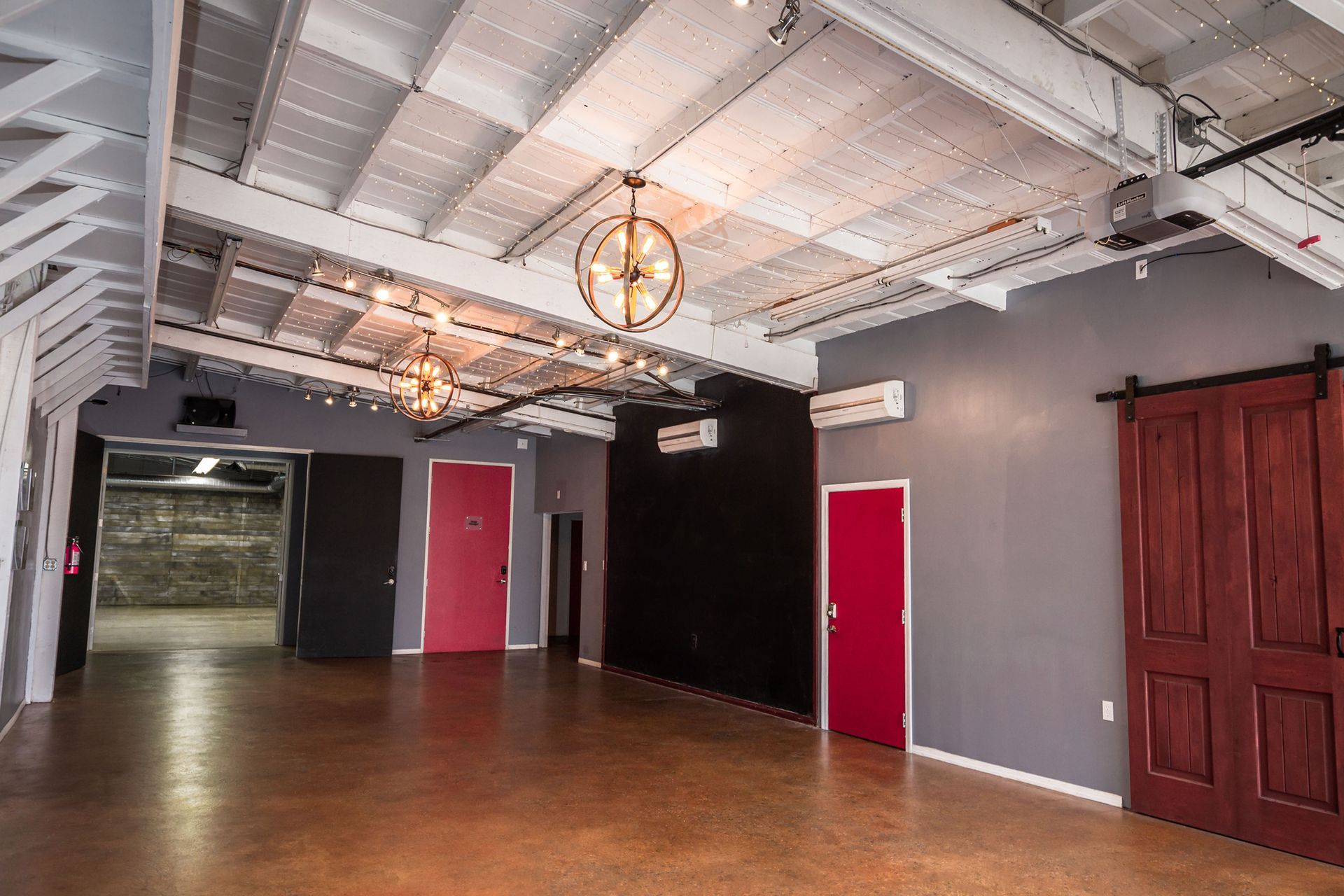A large empty room with sliding barn doors and a chandelier hanging from the ceiling.