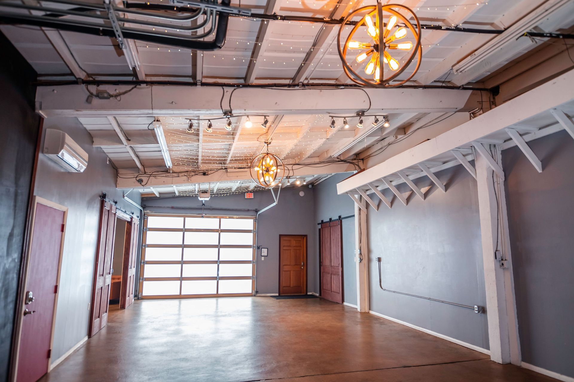 A large empty room with a garage door and a chandelier hanging from the ceiling.