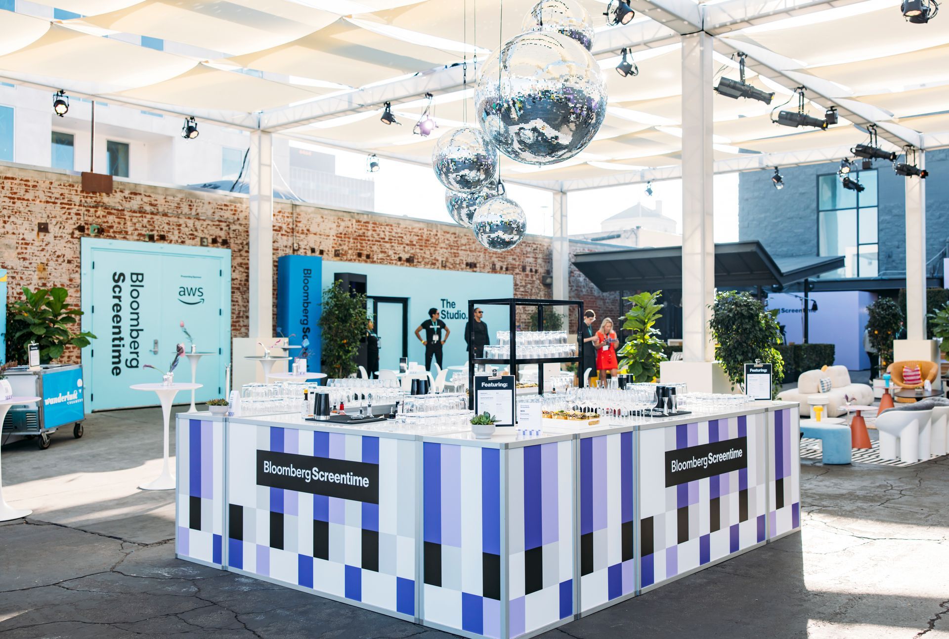 An outdoor pop-up event space features a bar with blue, black, and white checkered patterns under hanging disco balls.