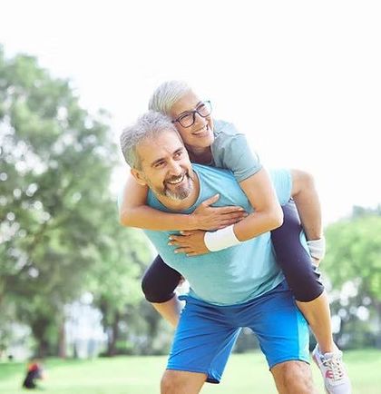 Smiling man giving a piggyback ride to a smiling child in a park