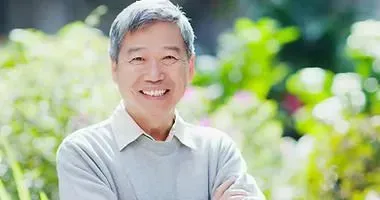 Smiling man in a light gray sweater standing outdoors, smiling with his relines.