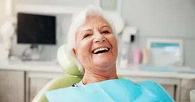 Smiling person reclining in a dental chair with a blue bib in a bright clinic within immediate denture work completed.
