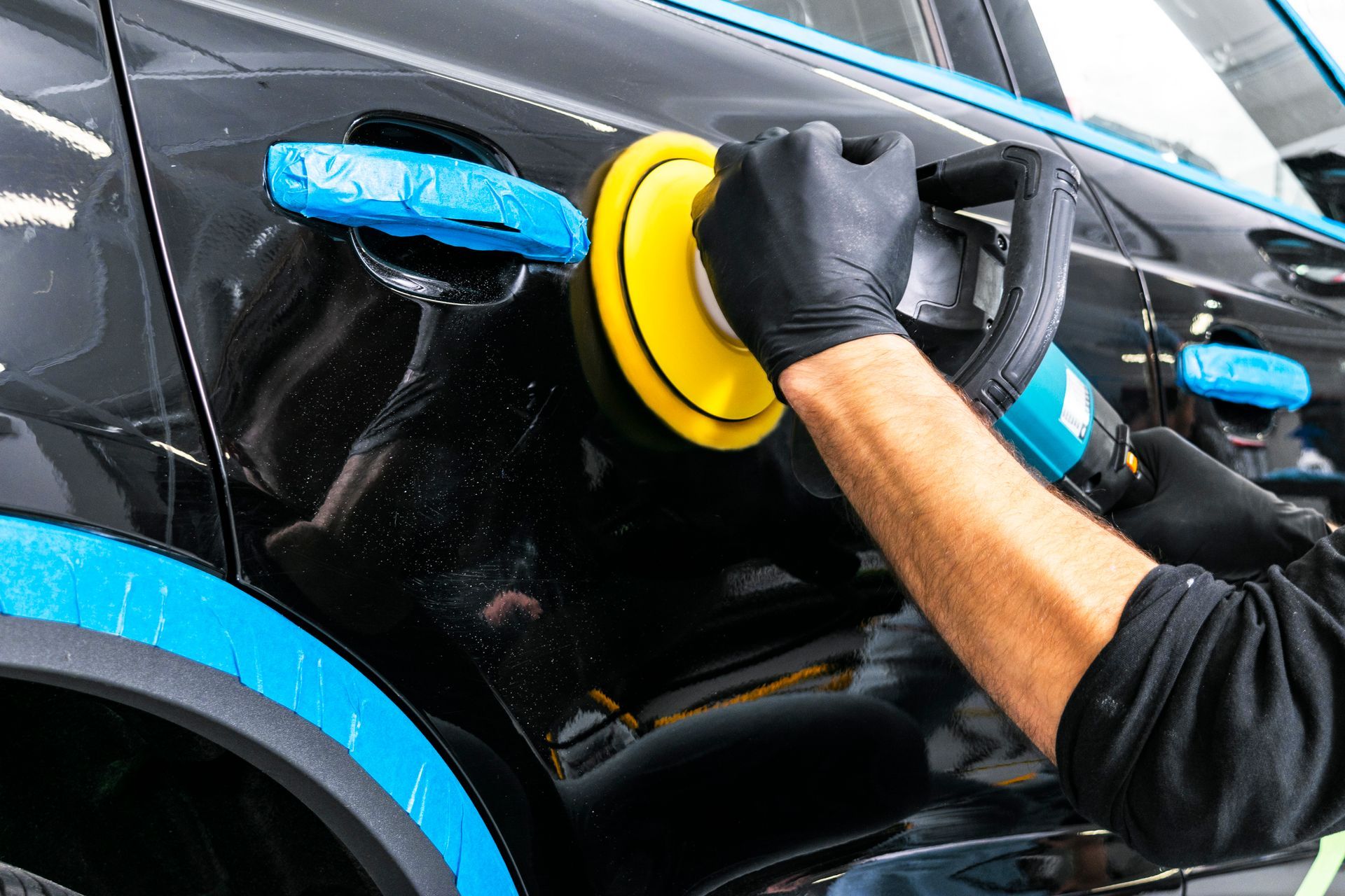 A man is polishing a black car with a machine.