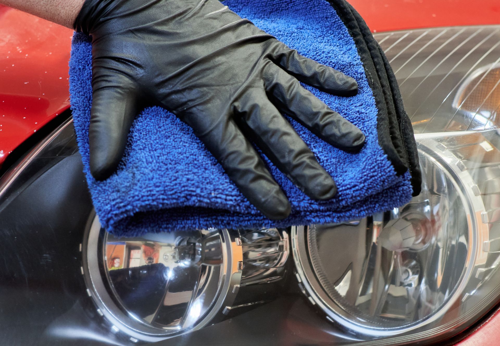 A person wearing black gloves is cleaning a car headlight with a blue towel.