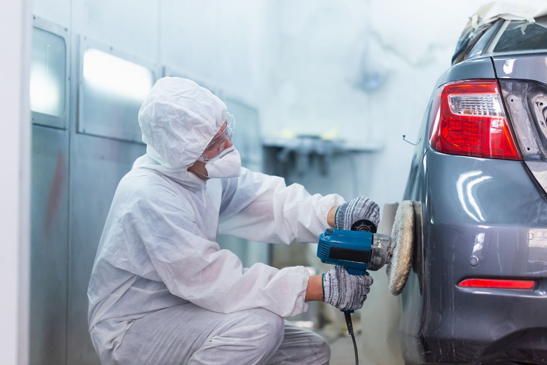 A man is polishing a car with a machine in a garage.
