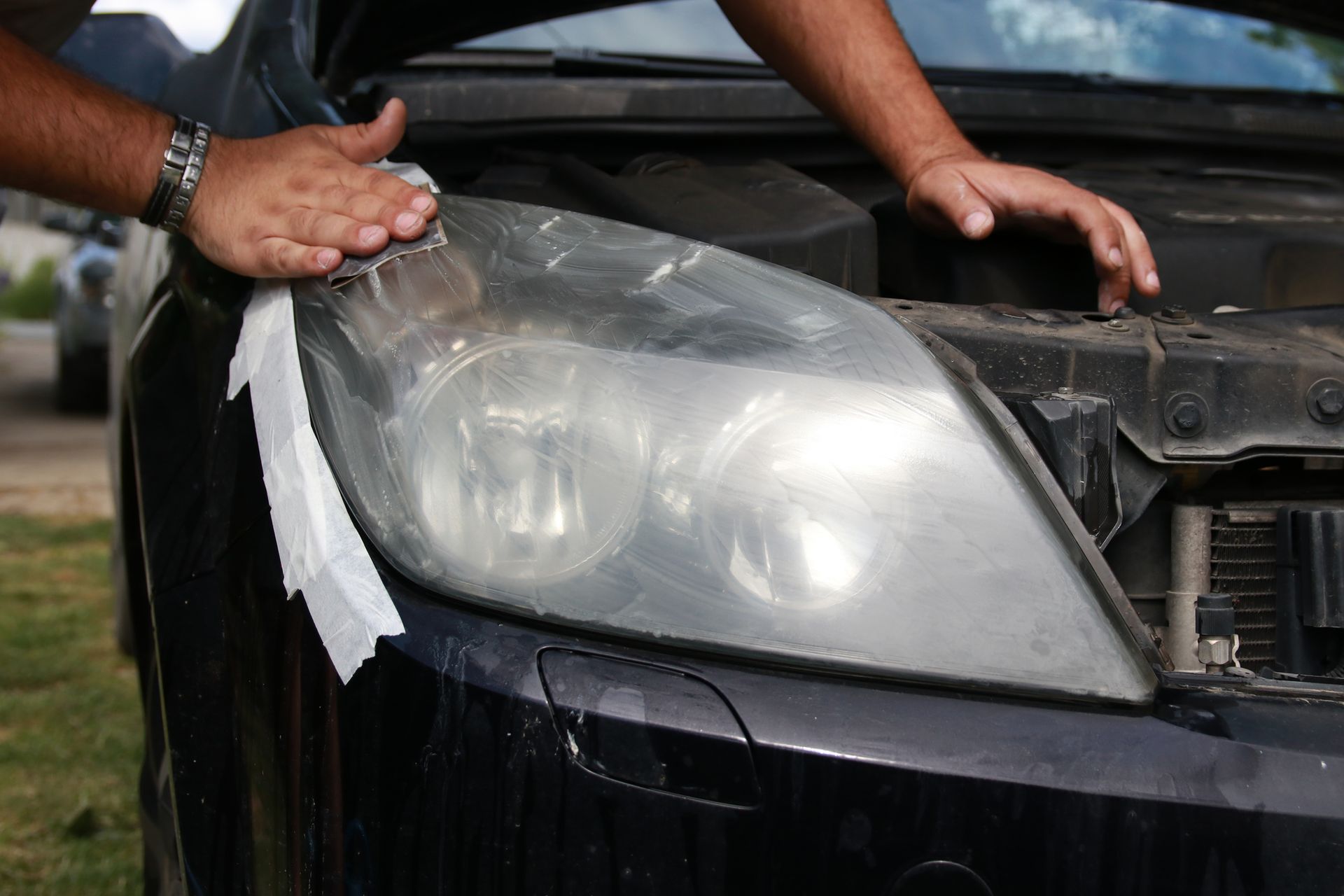 A man is cleaning the headlight of a car with a paper towel.