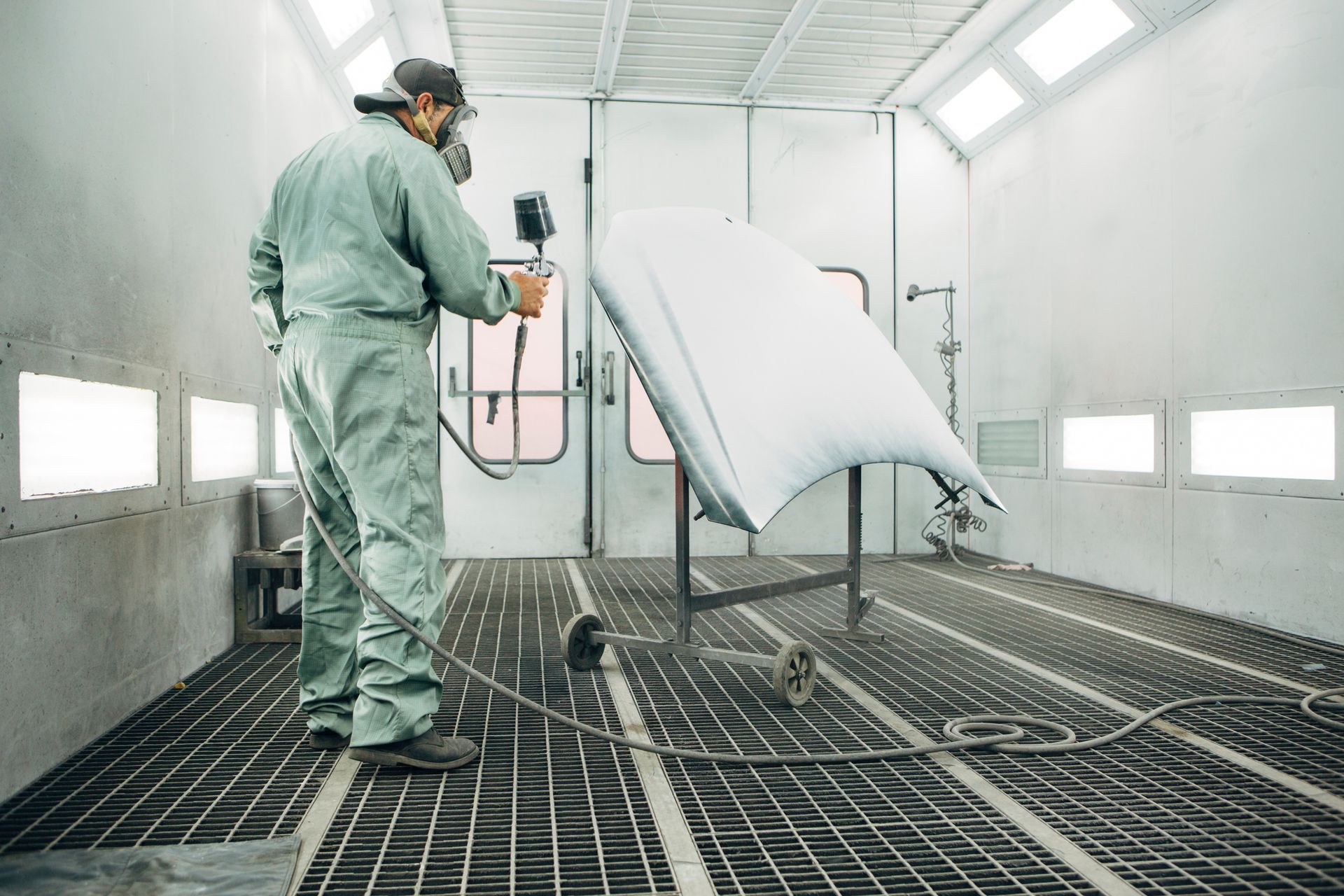 A man is painting a piece of metal in a paint booth.