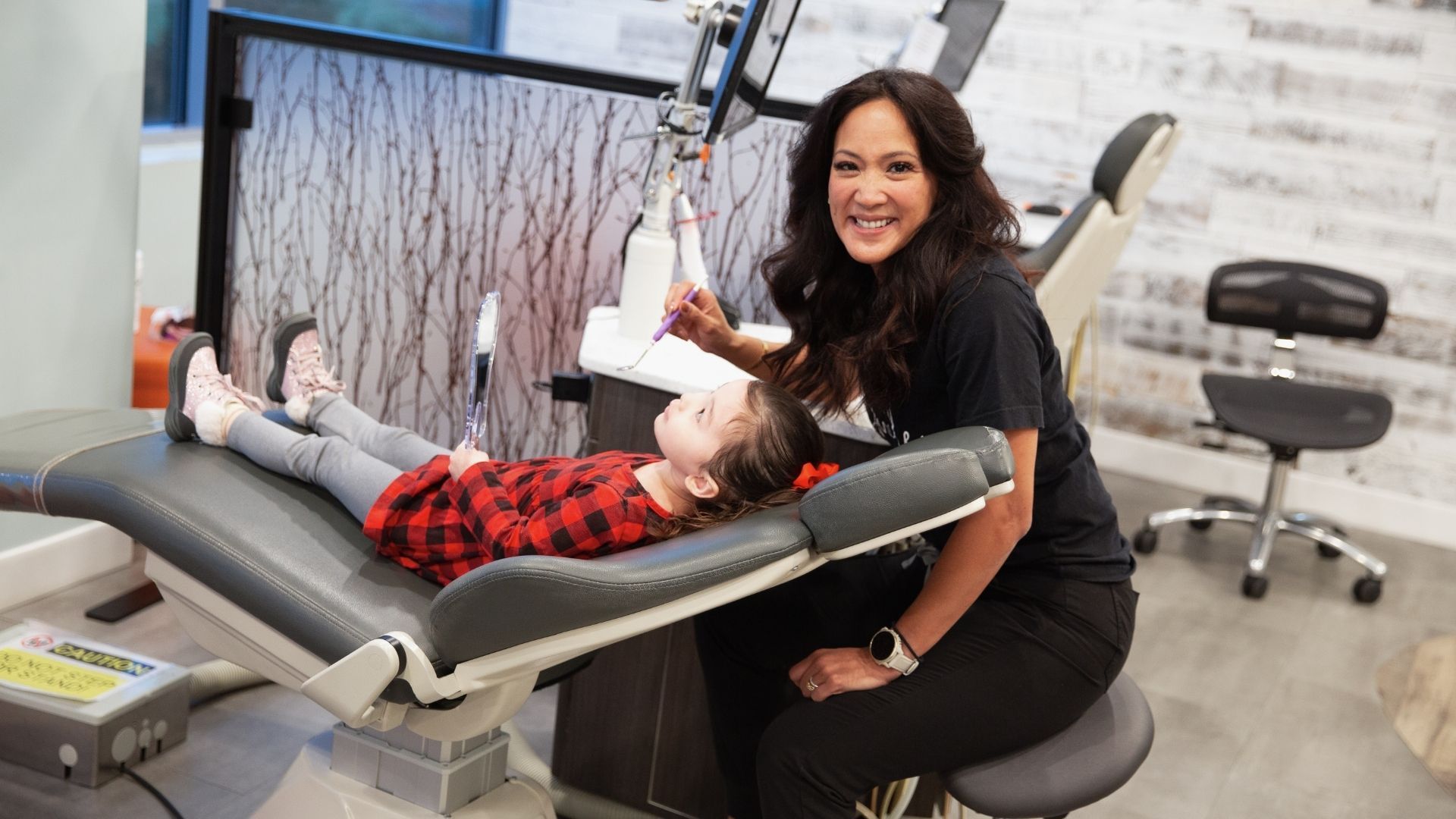 Dentist examining a young girl's teeth in a dental office. The girl smiles, while the dentist sits and smiles.
