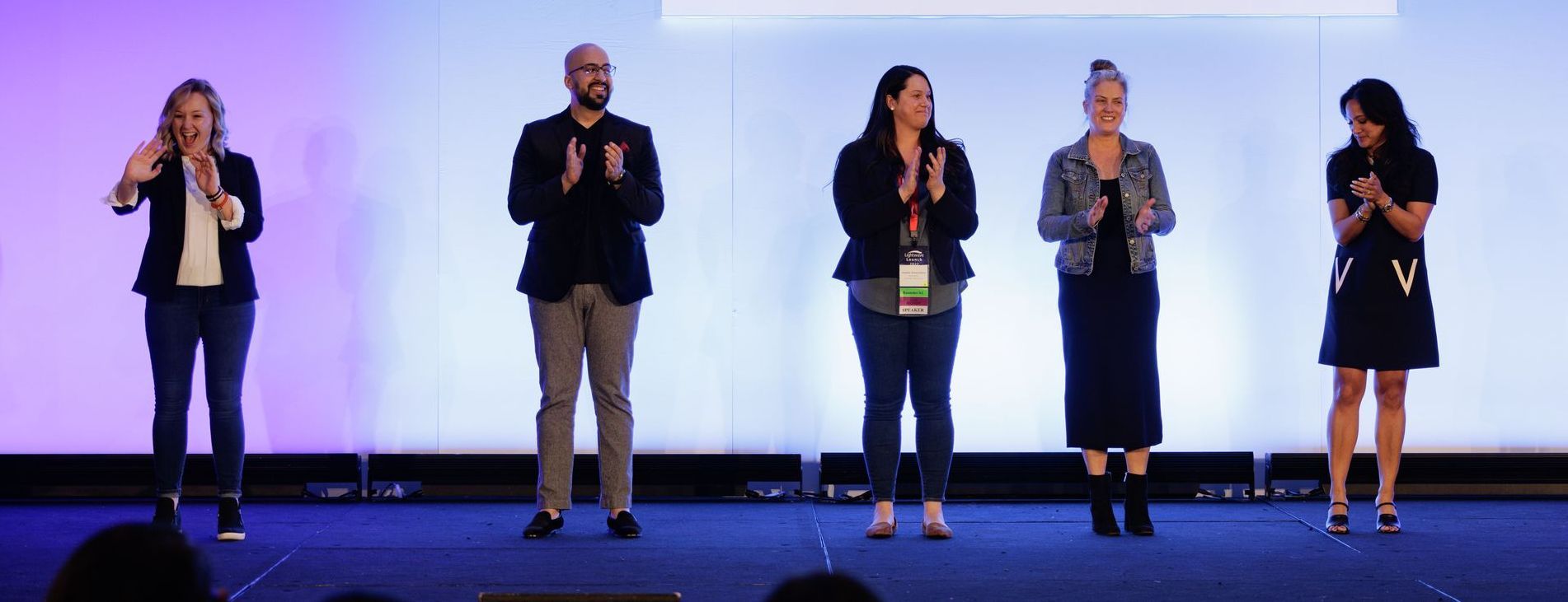 Five people on stage clapping, a light blue and white background.