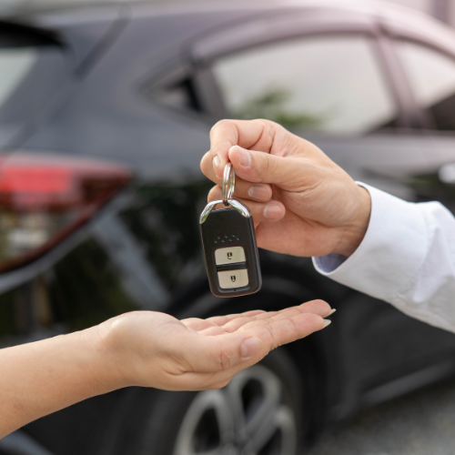 Car keys being handed over in front of a black car