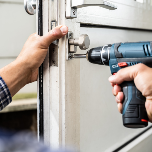 Hands using a cordless drill to install a door lock on a white door frame